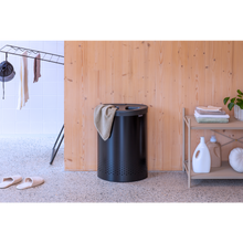 Load image into Gallery viewer, Lifestyle image of Brabantia Laundry Bin with Inner Removable Bag - 55 Liters, Selector - Matt Black.